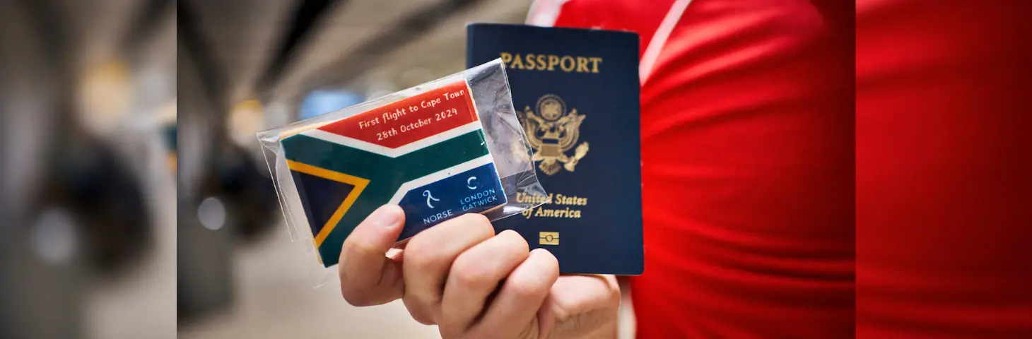 Image of a passenger holding a 'First Flight to South Africa' badge with their passport