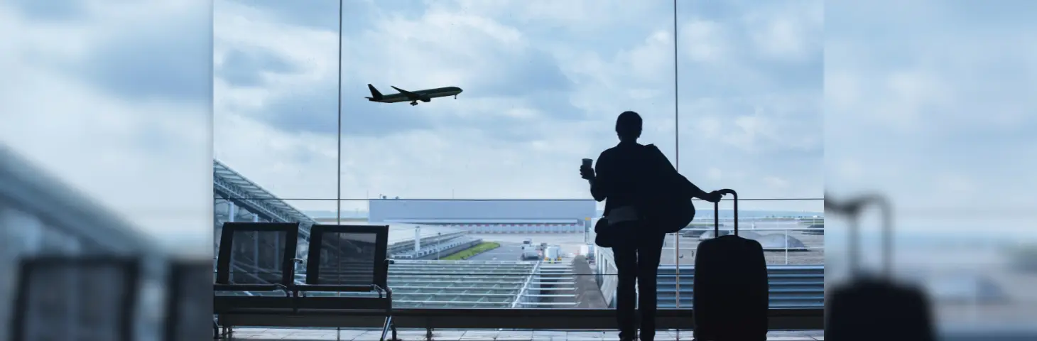 Image of a lady looking out of an airport window at a plane taking off